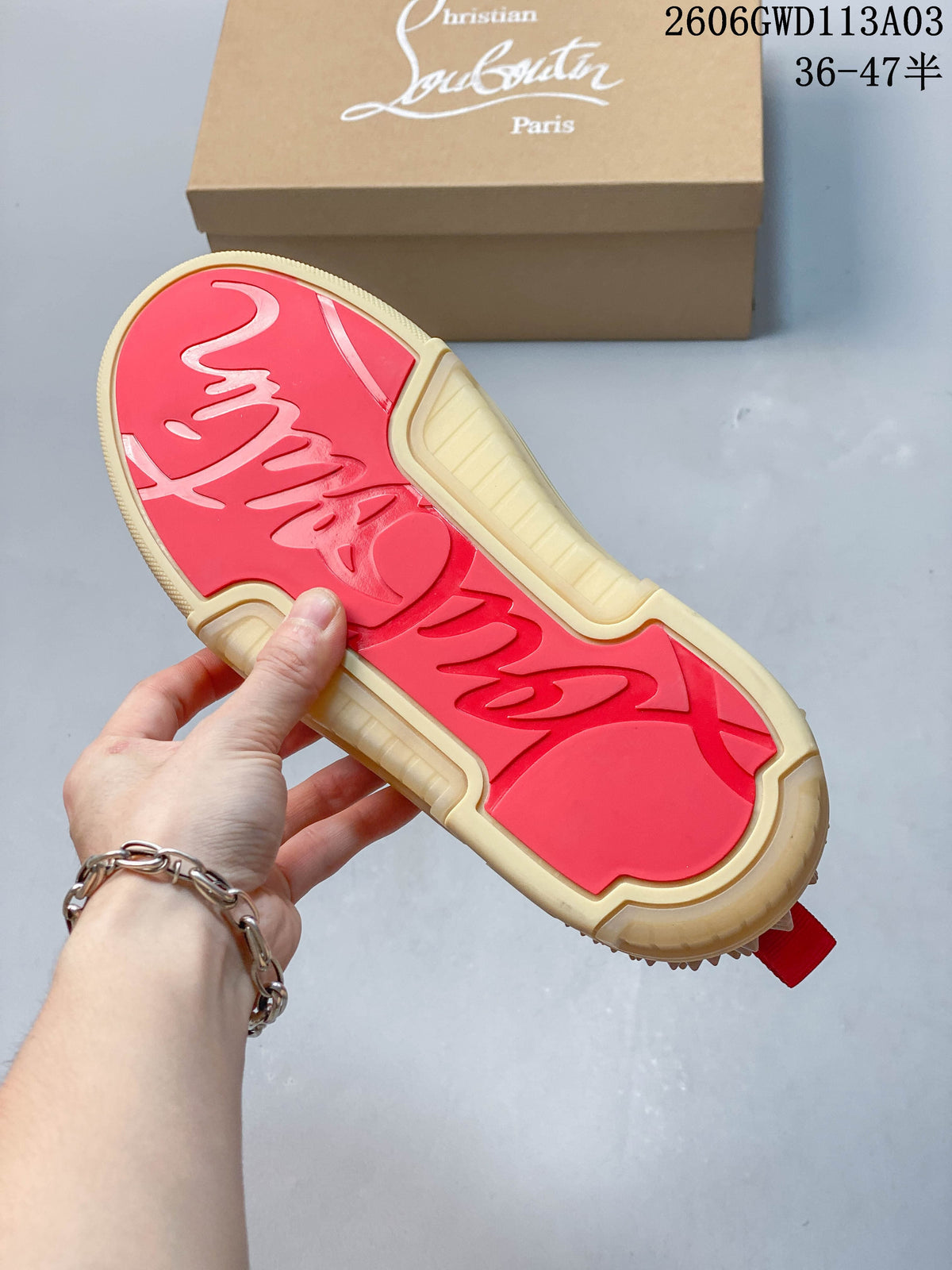 Underside of a sneaker showing a red outsole panel and beige sole, with the shoe box in the background