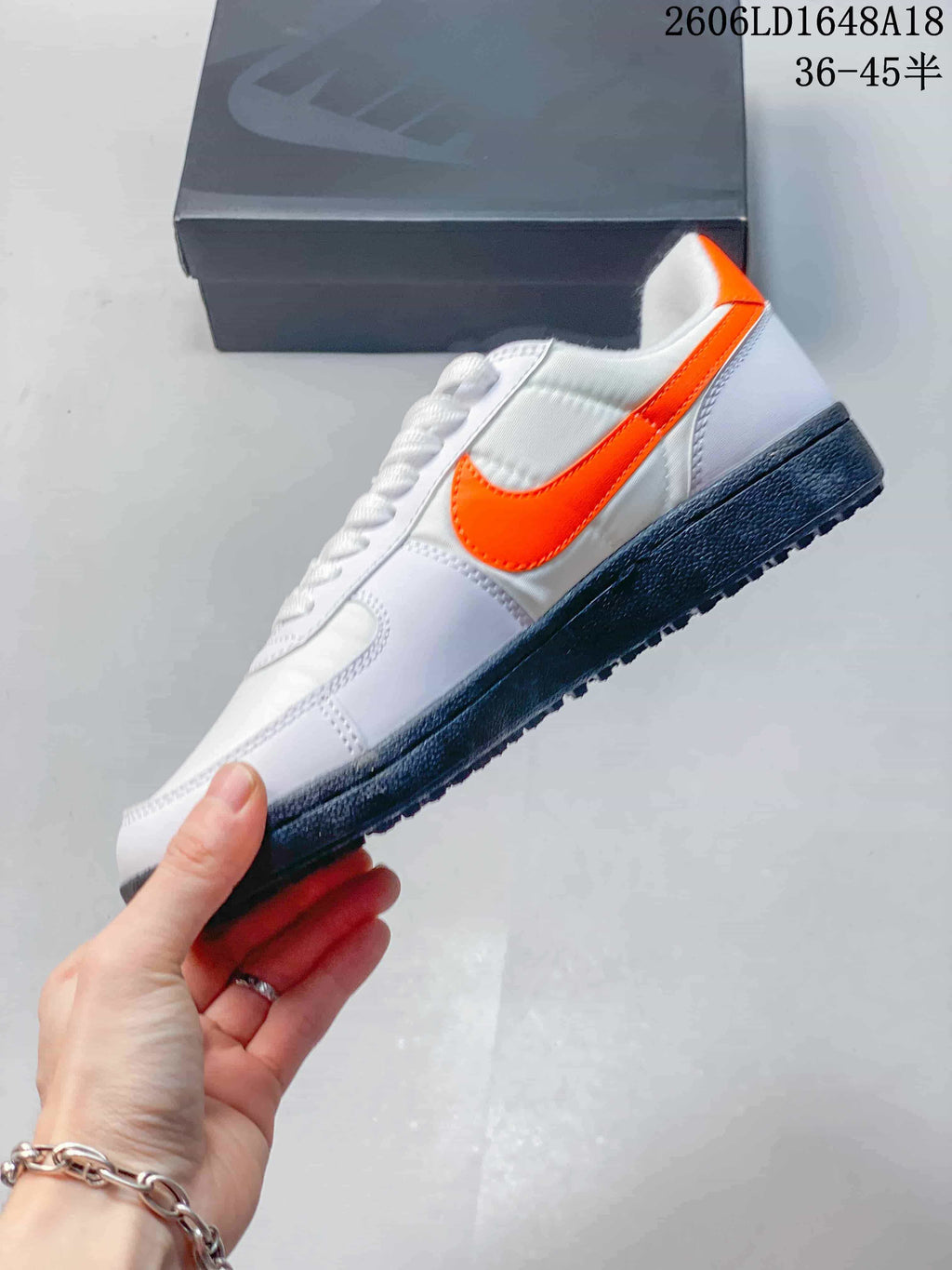 Side view of the white sneaker with bright orange Swoosh and dark outsole