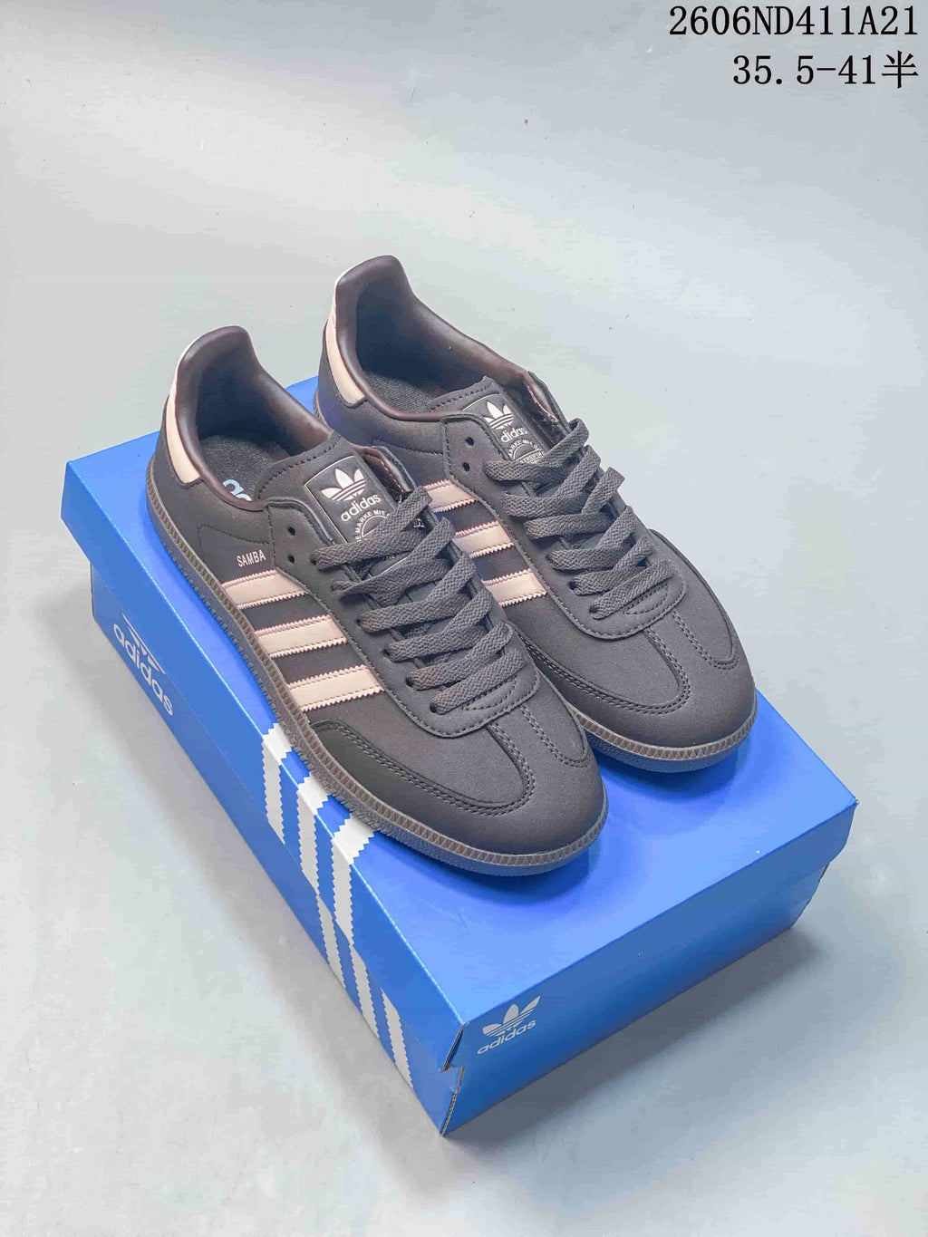Pair of charcoal Adidas low-top sneakers with pale pink stripes and heel accents, displayed on a blue shoe box.