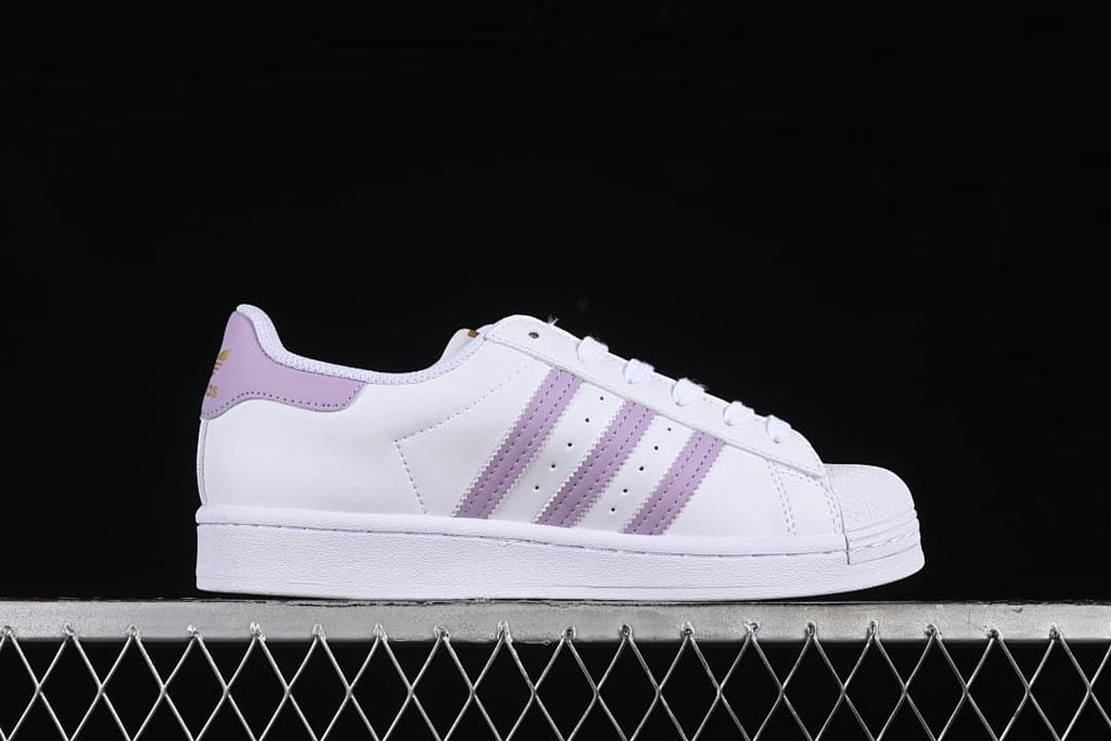 Side profile of a white Superstar sneaker with lavender stripes