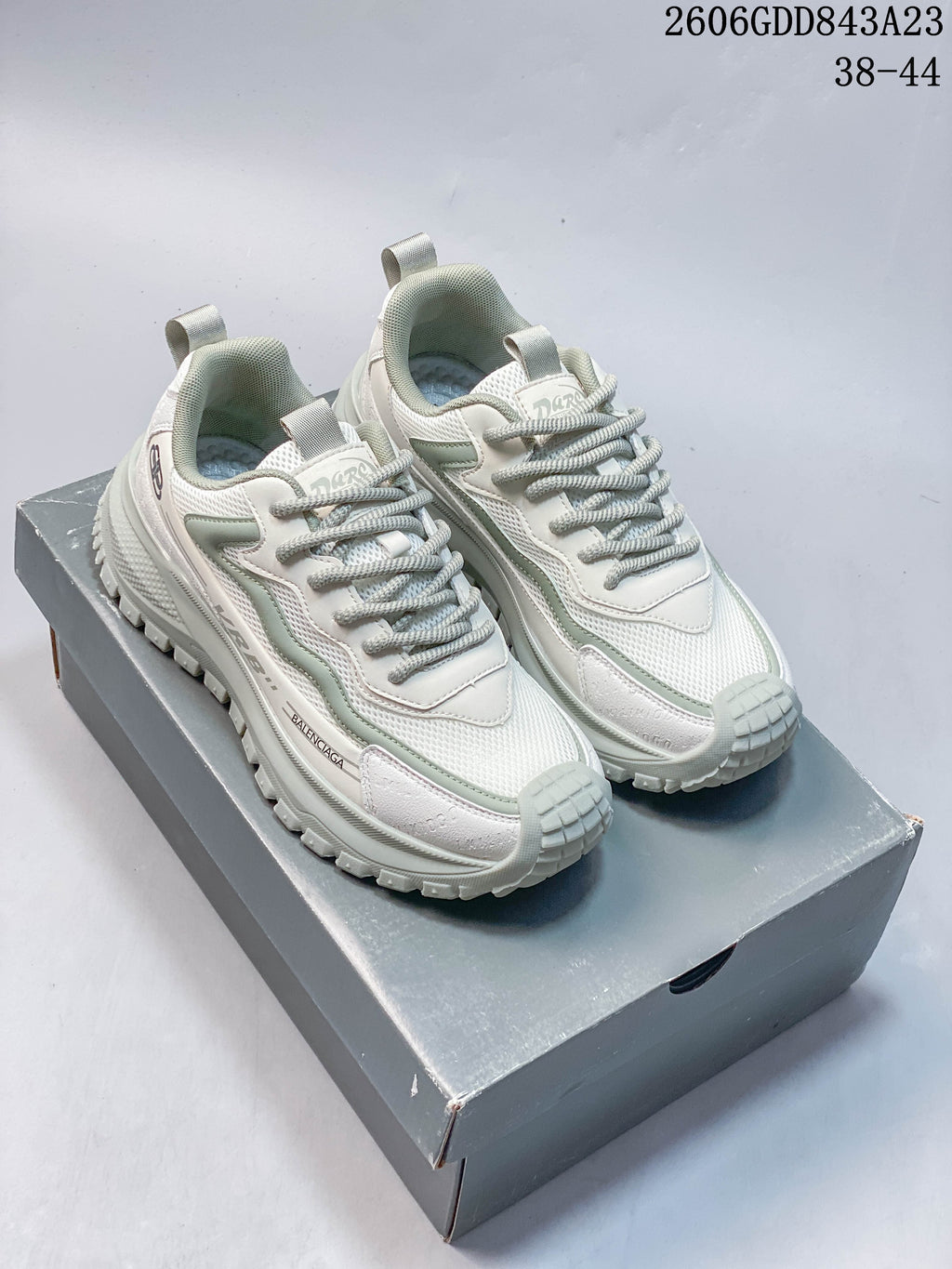 Pair of white and pale sage-green layered lace-up sneakers on a gray box