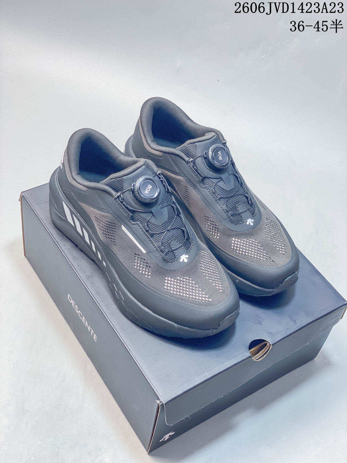 Pair of charcoal Descente Traxis sneakers with dial closures, shown on a shoe box.