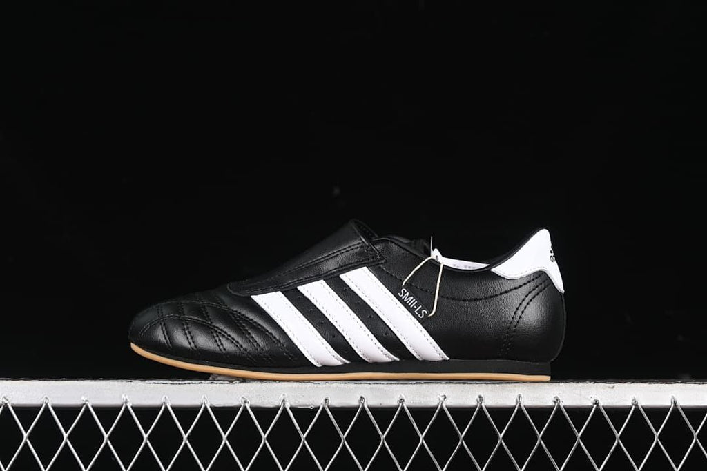 Side view of a black Adidas Taekwondo sneaker with white stripes and a gum-colored sole.
