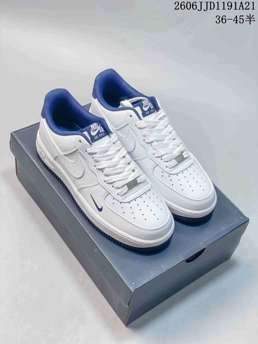 White low-top sneakers with blue collar lining and small blue Swoosh accents, shown on a shoebox.