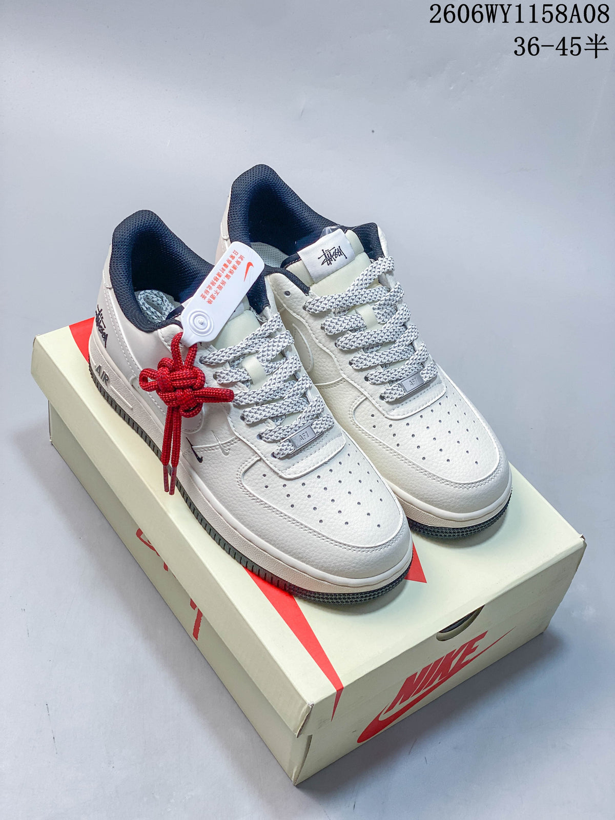 Pair of pale Nike Air Force 1 '07 low-top sneakers with navy accents, patterned gray laces, and red lace detail on a box.