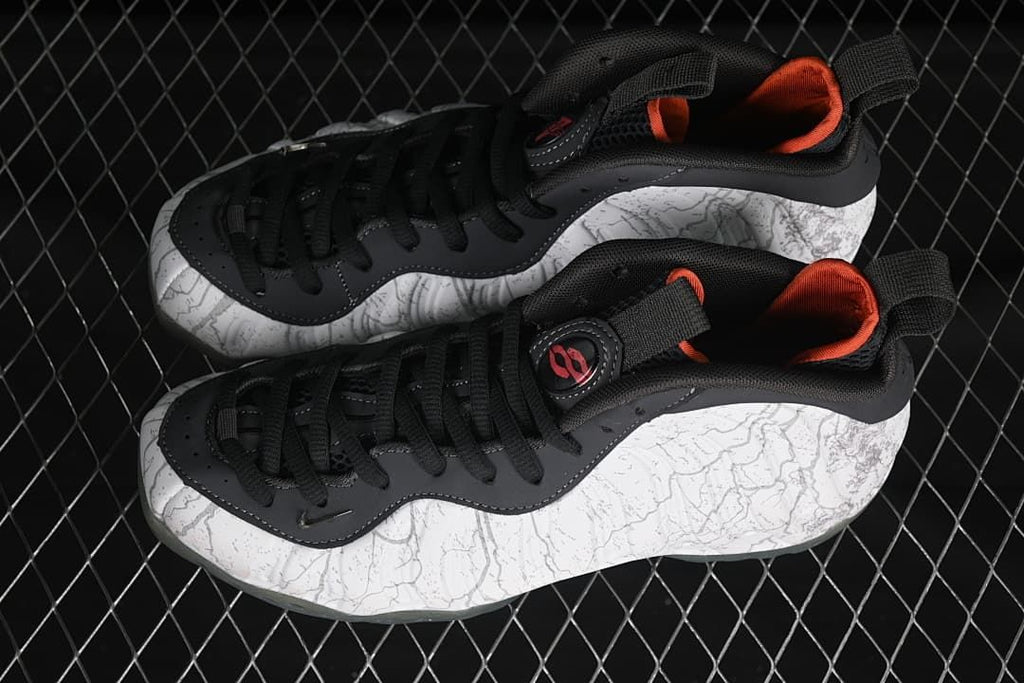 Pair of white and gray patterned sneakers with black laces and orange lining.