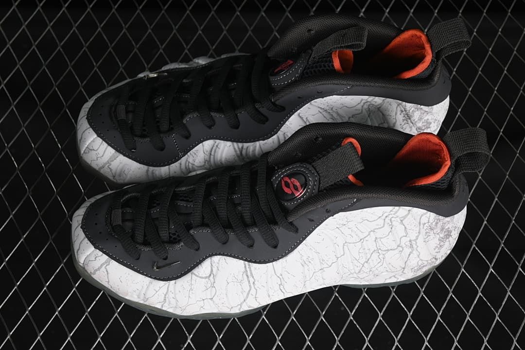 Pair of white and gray patterned sneakers with black laces and orange lining.