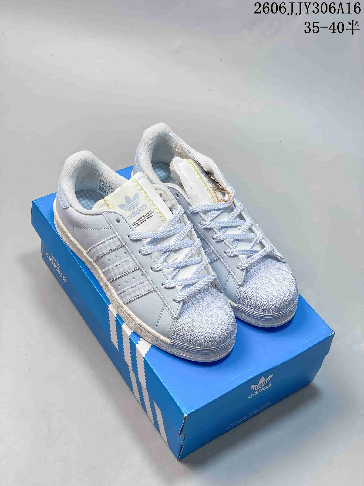 White and pale blue Adidas Superstar II sneakers shown on a blue shoebox