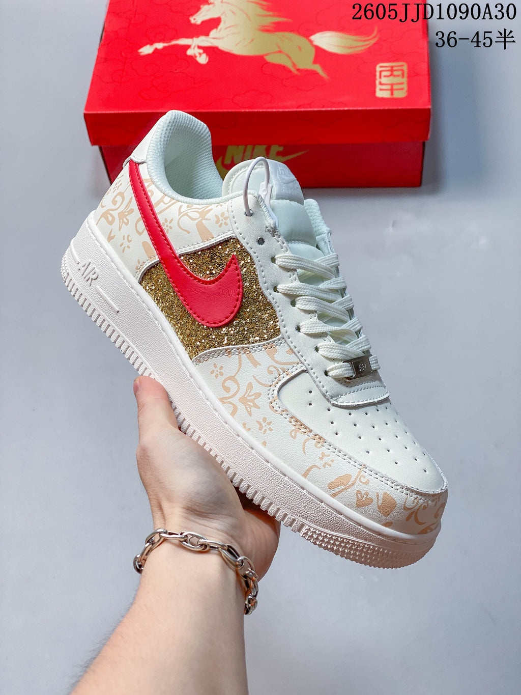 Angled side view of the ivory sneaker with gold glitter panels and red Swoosh accents