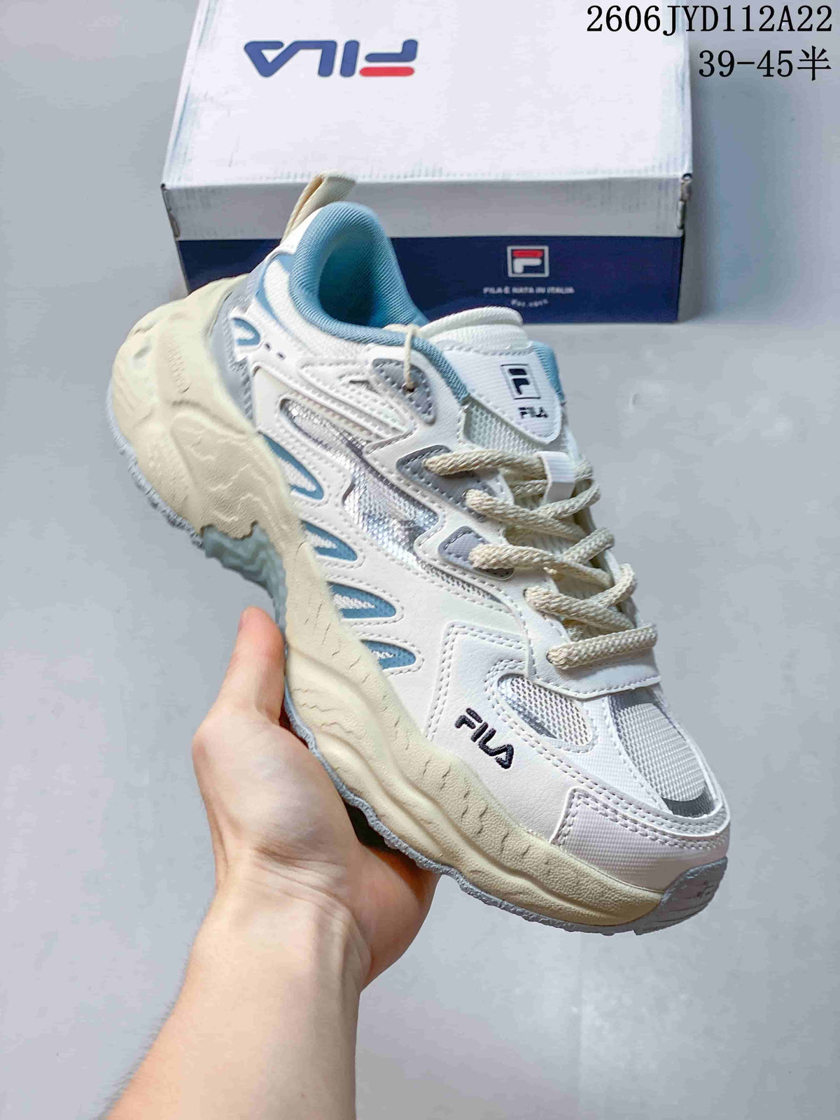 Angled view of a white FILA sneaker with mesh panels, light blue accents, and a chunky cream-colored sole.