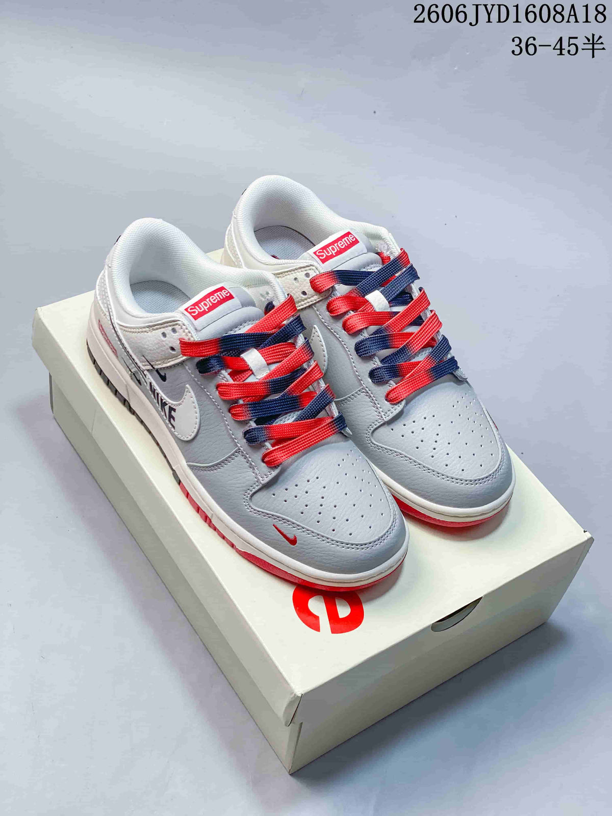 Pair of grey and white low-top sneakers with red and navy laces on a Supreme-branded box.