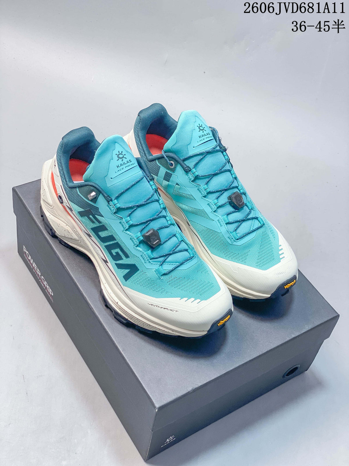 Pair of turquoise and white Kailas FUGA trail shoes with dial-adjustable laces, shown on a box.
