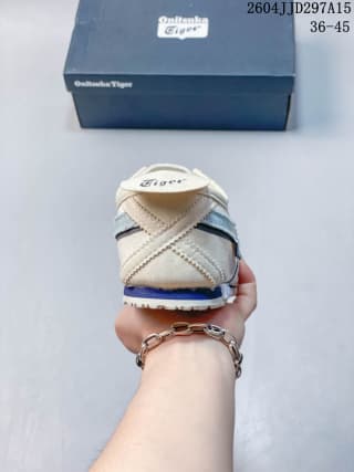 Rear view of the cream and blue Onitsuka Tiger sneaker held in front of its branded box.