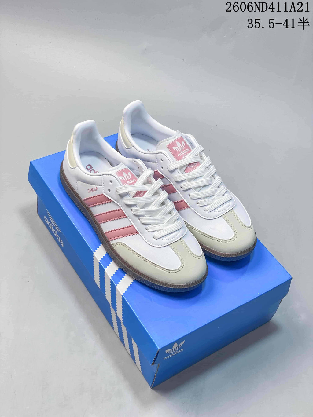 Pair of white Adidas sneakers with pink stripes and pale toe panels, displayed on a blue shoe box
