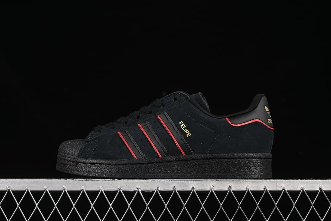 Side view of a black adidas Superstar-style sneaker with red accents and gold details