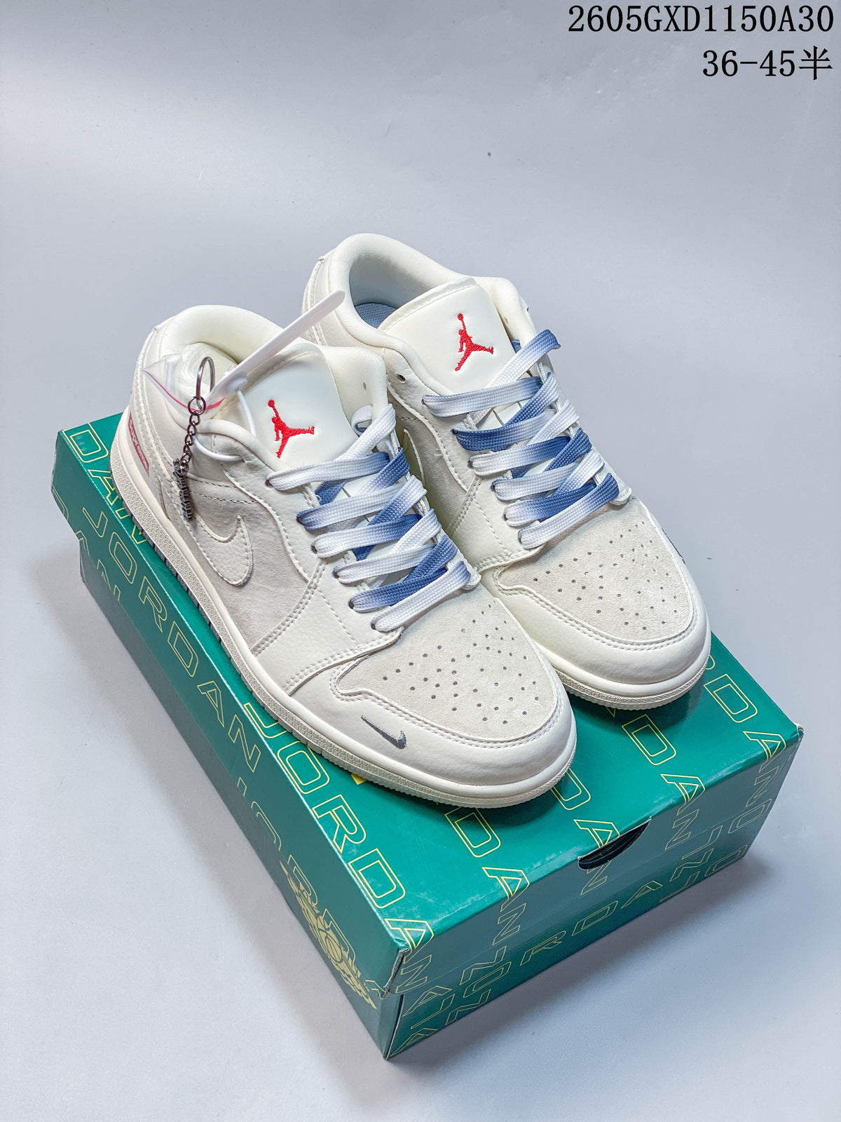 Off-white and light gray low-top sneakers with blue-and-white laces and a small charm, shown on a green box.