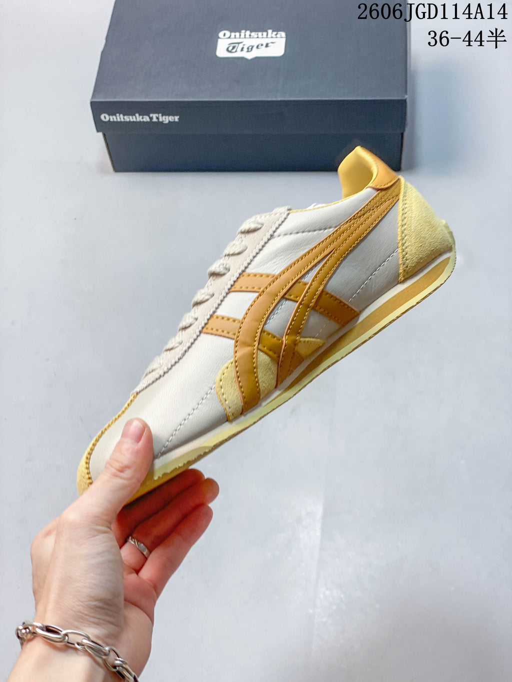 Side profile of a light neutral low-top sneaker with mustard-gold stripes and pale yellow accents