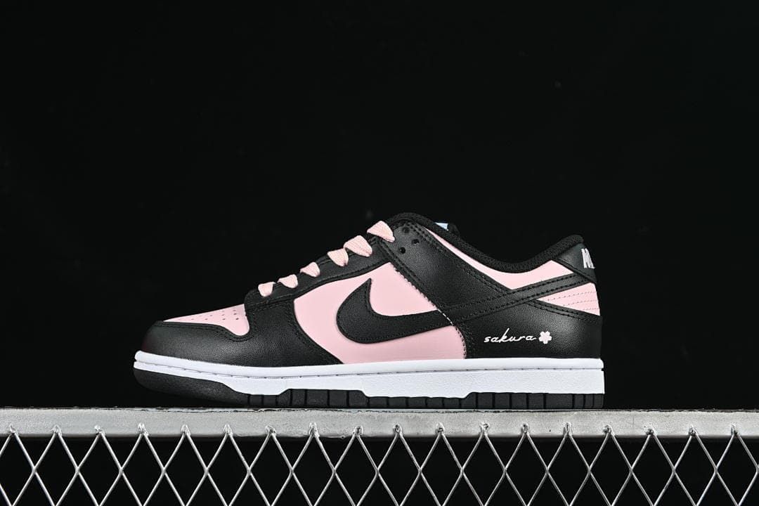 Side profile of a black and pale pink low-top Dunk sneaker with sakura-style heel embroidery