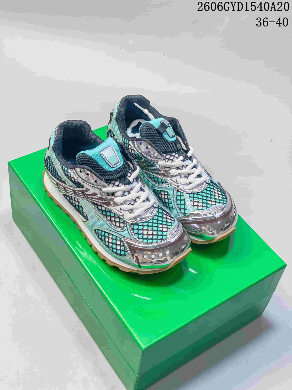 Pair of turquoise, black, and silver Bottega Veneta Orbit lace-up runner sneakers on a green box