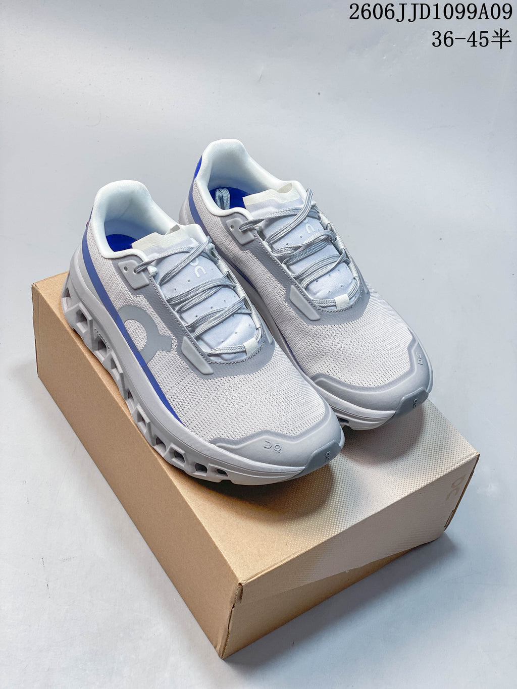Pair of white and light gray On Cloudmonster Void shoes with blue accents and open-channel soles.