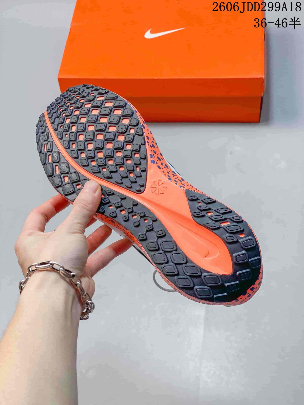 View of the patterned dark outsole and orange midsole of a white Nike running shoe.