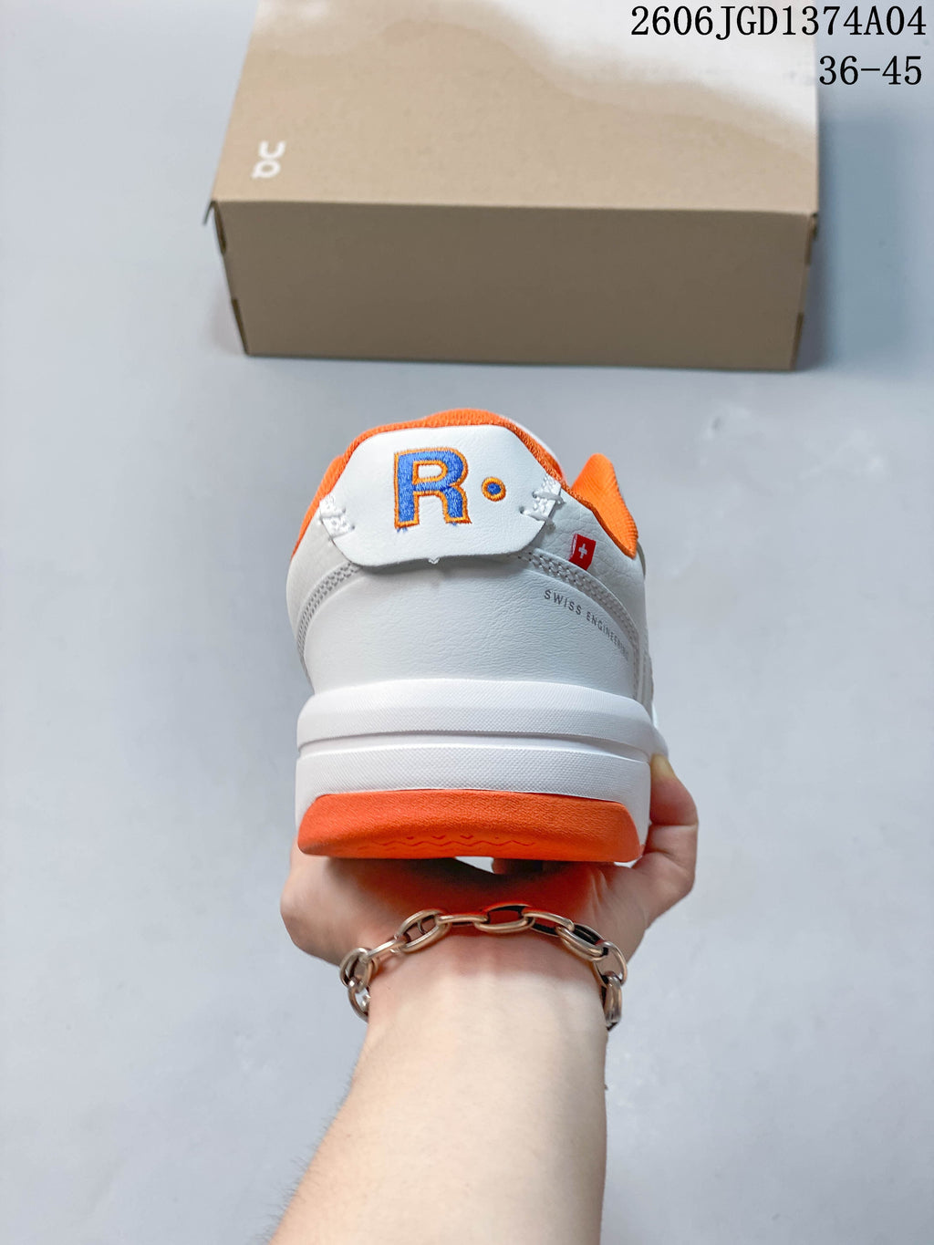 Rear view of the white sneaker with orange heel accent and contrasting embroidered detail