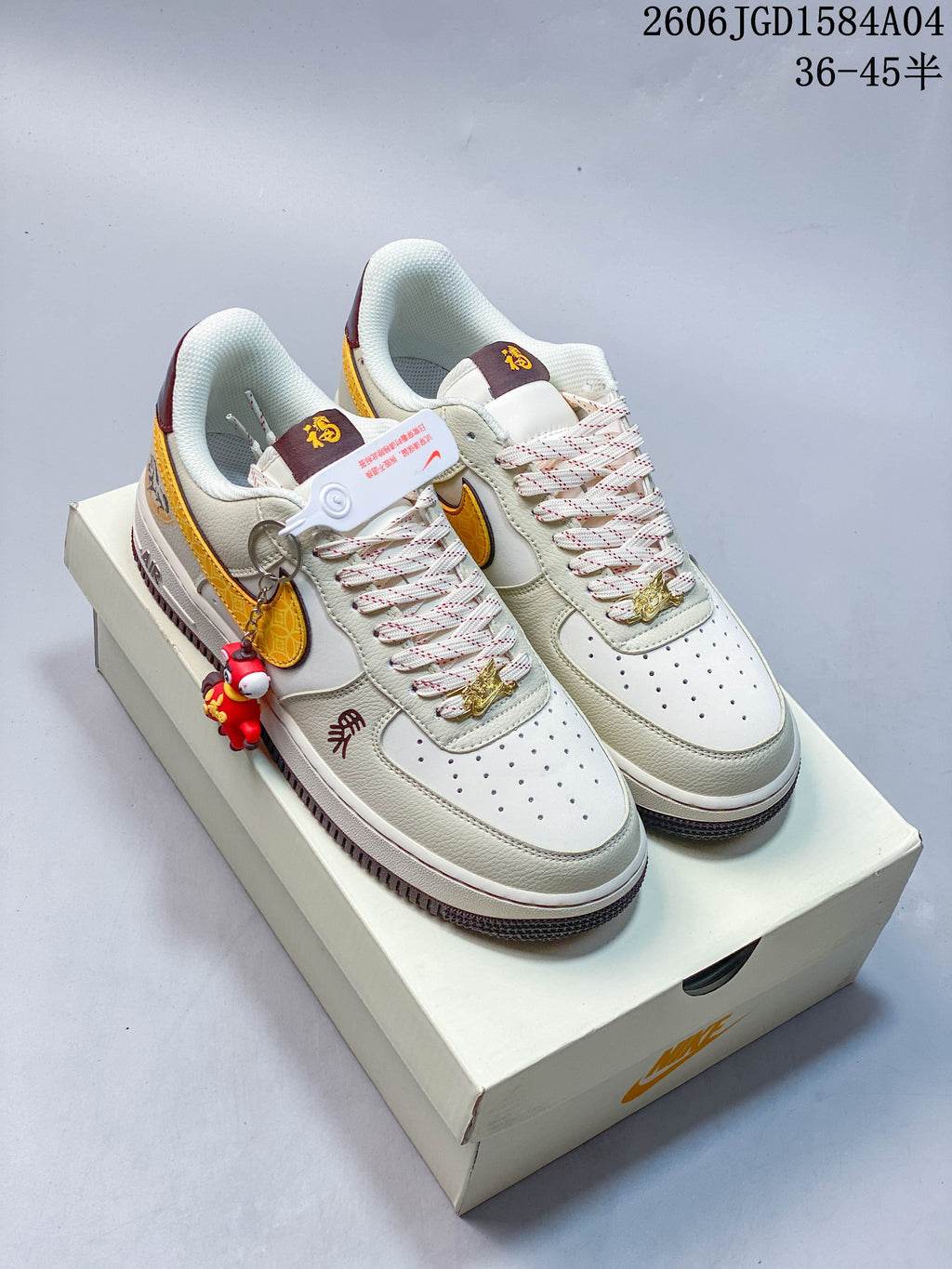 Pair of ivory and gold low-top sneakers with burgundy accents and a red hanging figure accessory