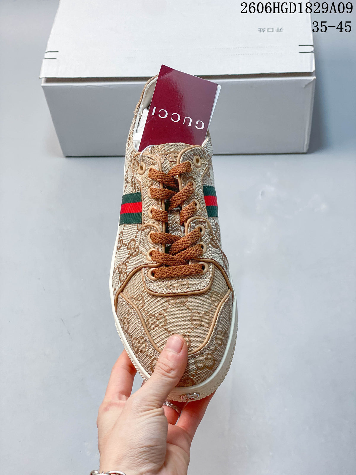Front view of a beige GG-pattern sneaker with brown laces and a green and red stripe