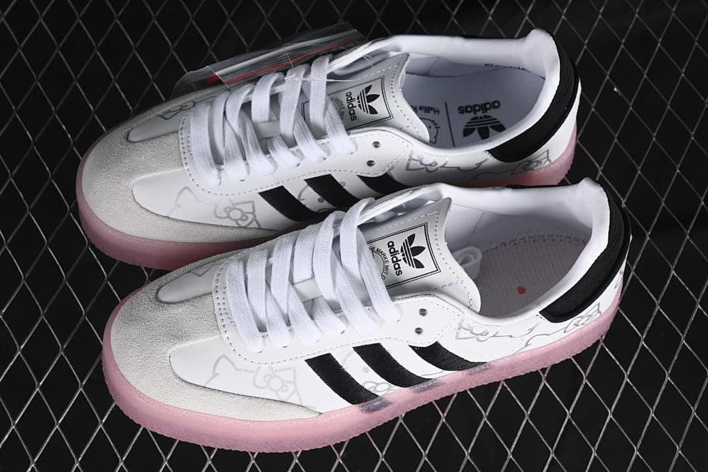 Pair of white adidas Samba W sneakers with black stripes, Hello Kitty graphics, and pink soles.