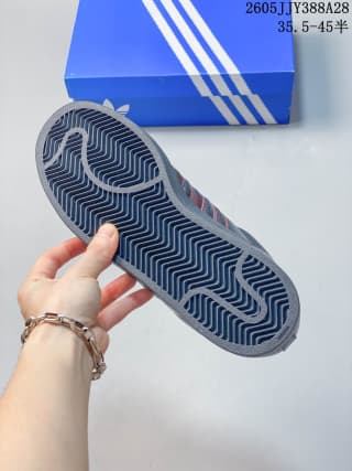 Outsole of a dark adidas Originals Superstar 2 sneaker held above a blue shoe box