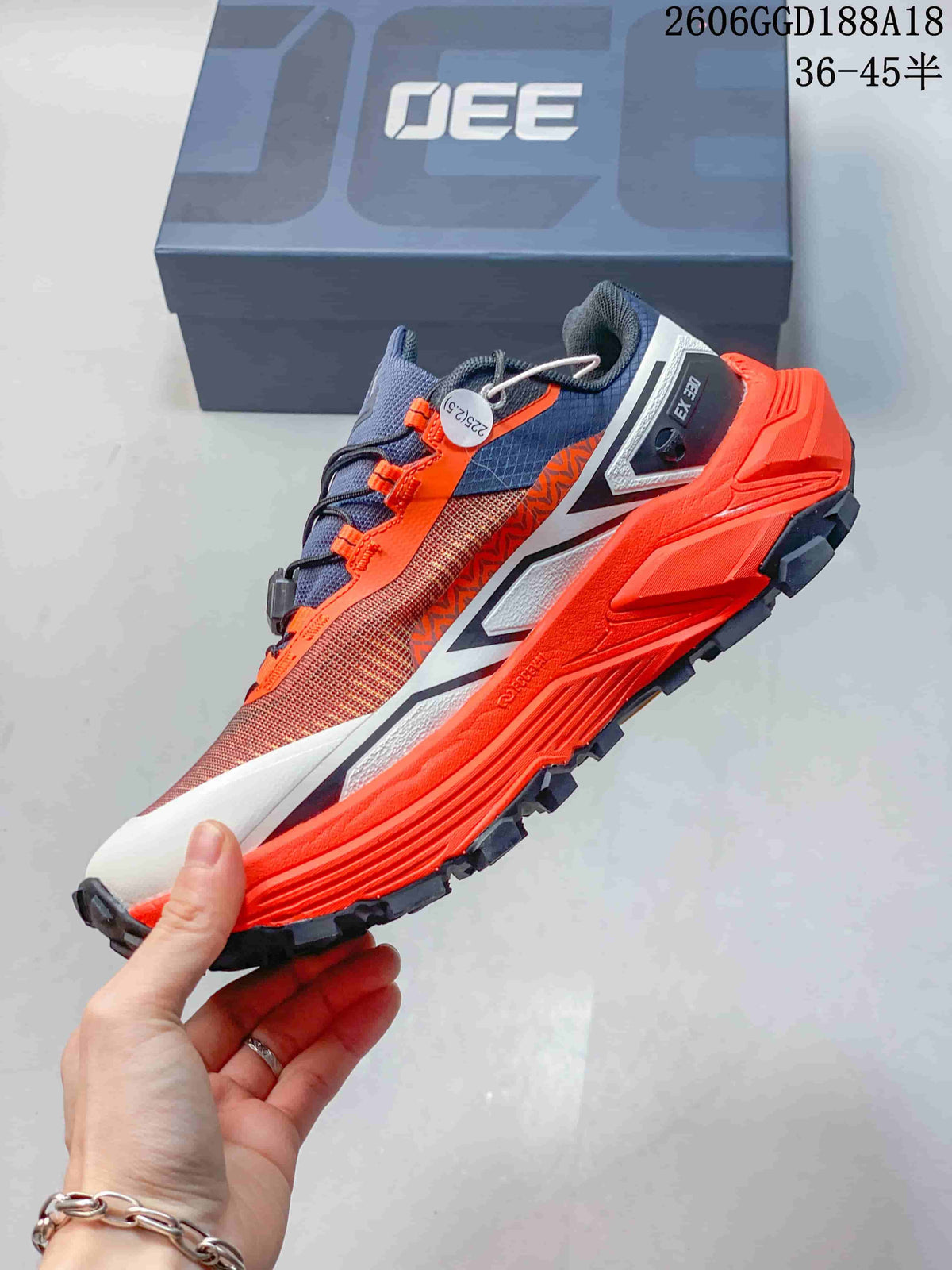 Side view of the trail shoe with orange midsole, dark lugs, and contrasting overlays
