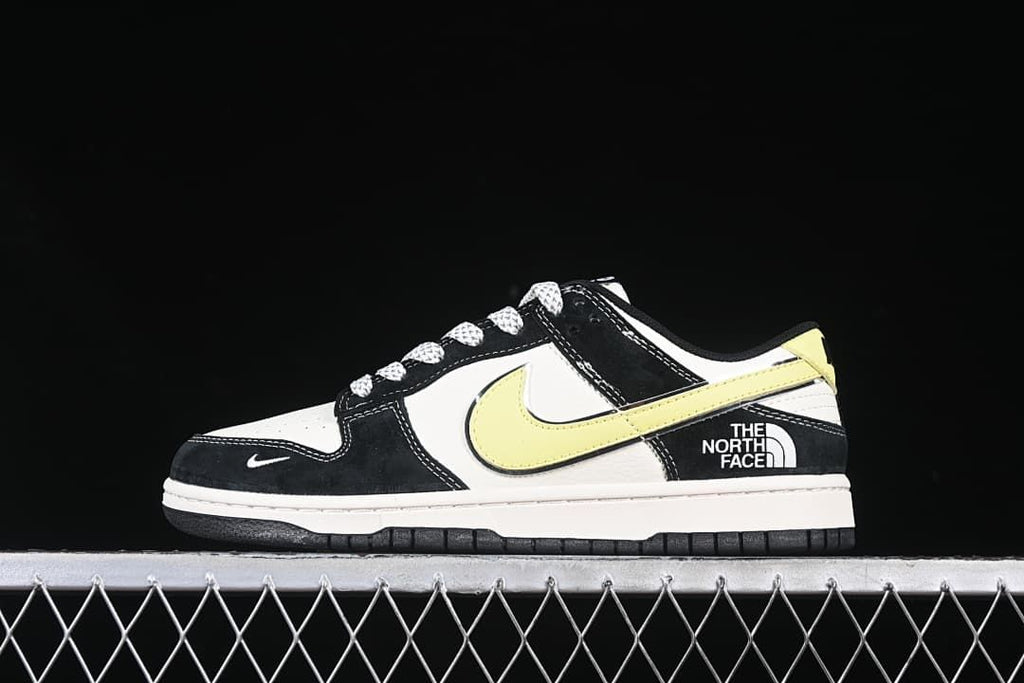 Side view of a black and white low-top sneaker with a pale yellow swoosh and The North Face heel branding.