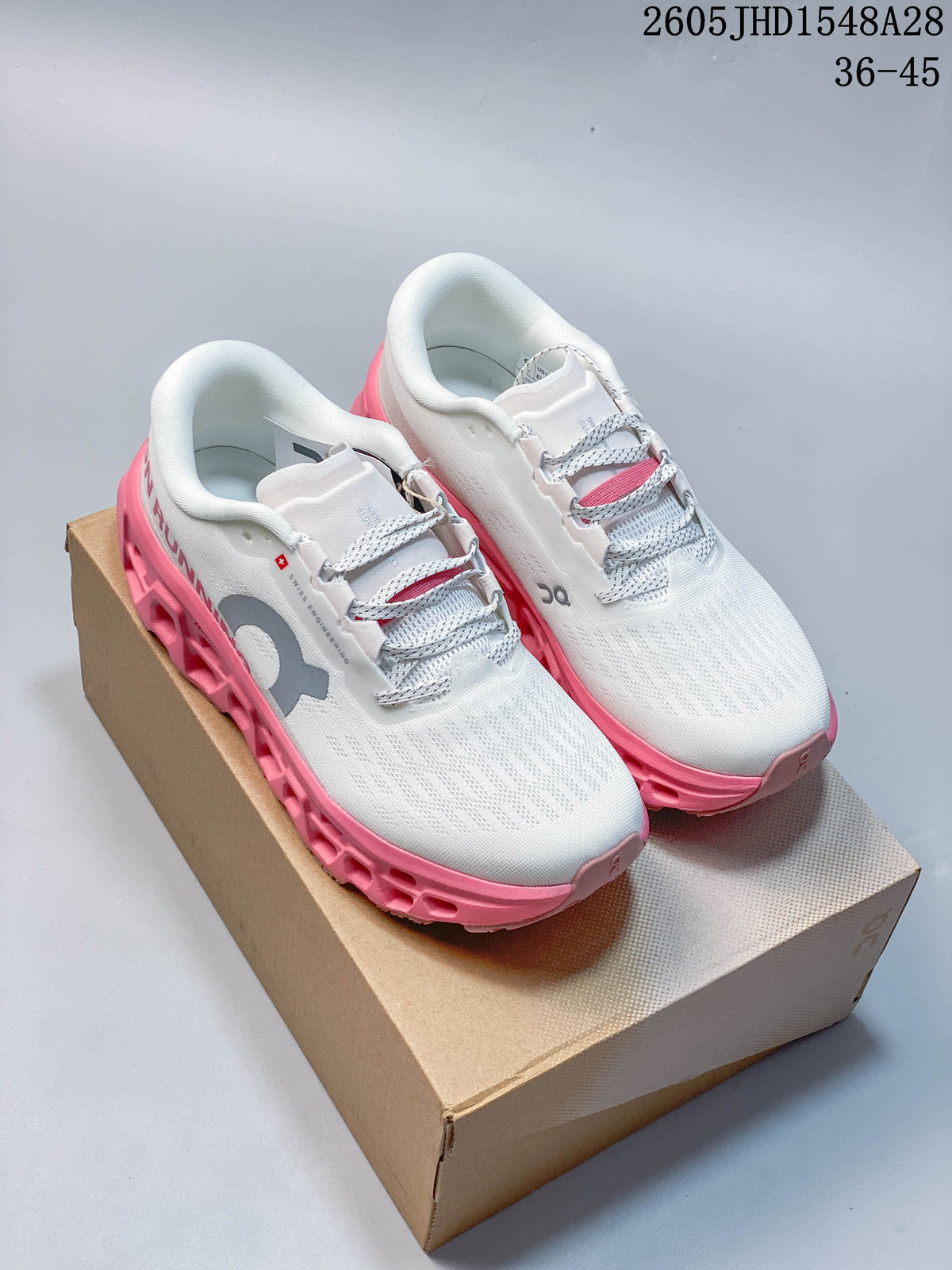 Pair of white On Cloudmonster 3 shoes with gray logos and pink soles, displayed on a box