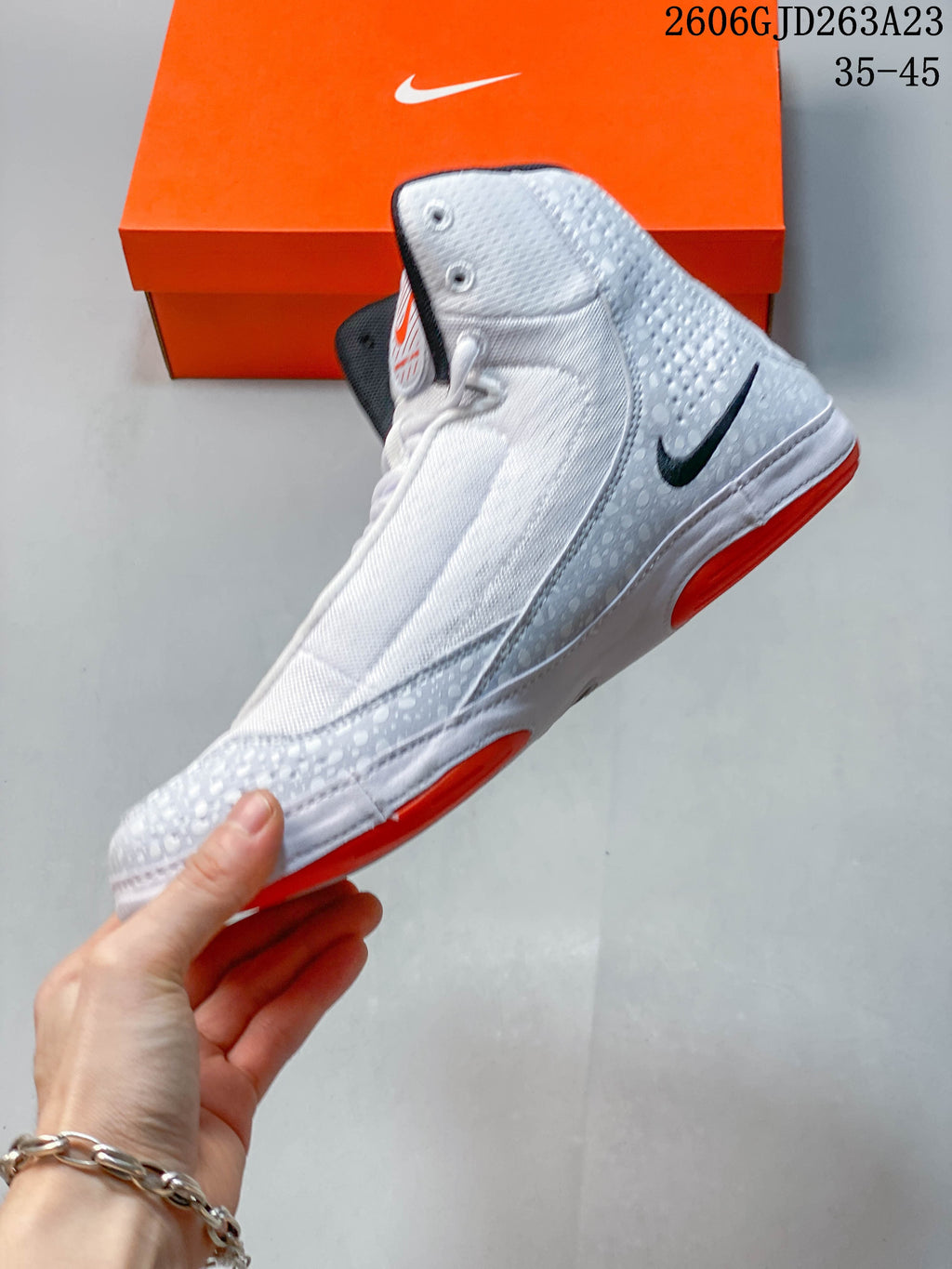 Side view of a white and light gray Nike Inflict 4 high-top shoe with black swoosh and orange outsole accents.