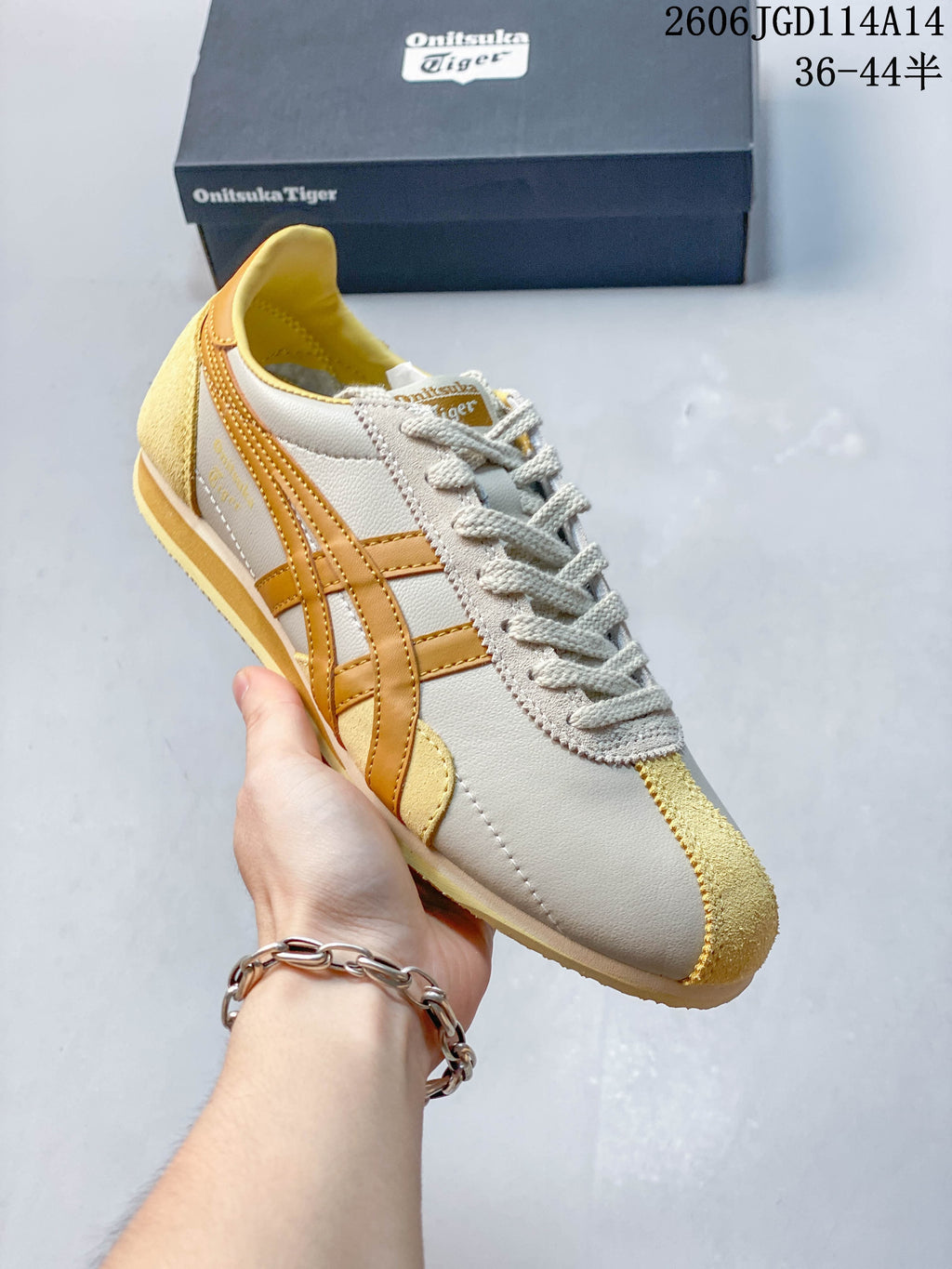 Angled view of a light neutral Onitsuka Tiger sneaker with mustard-gold stripes