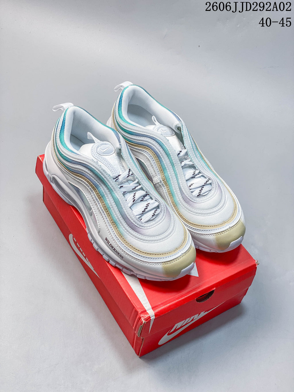 Pair of white Nike Air Max 97 sneakers with aqua and pale gold accents, shown on a red shoe box