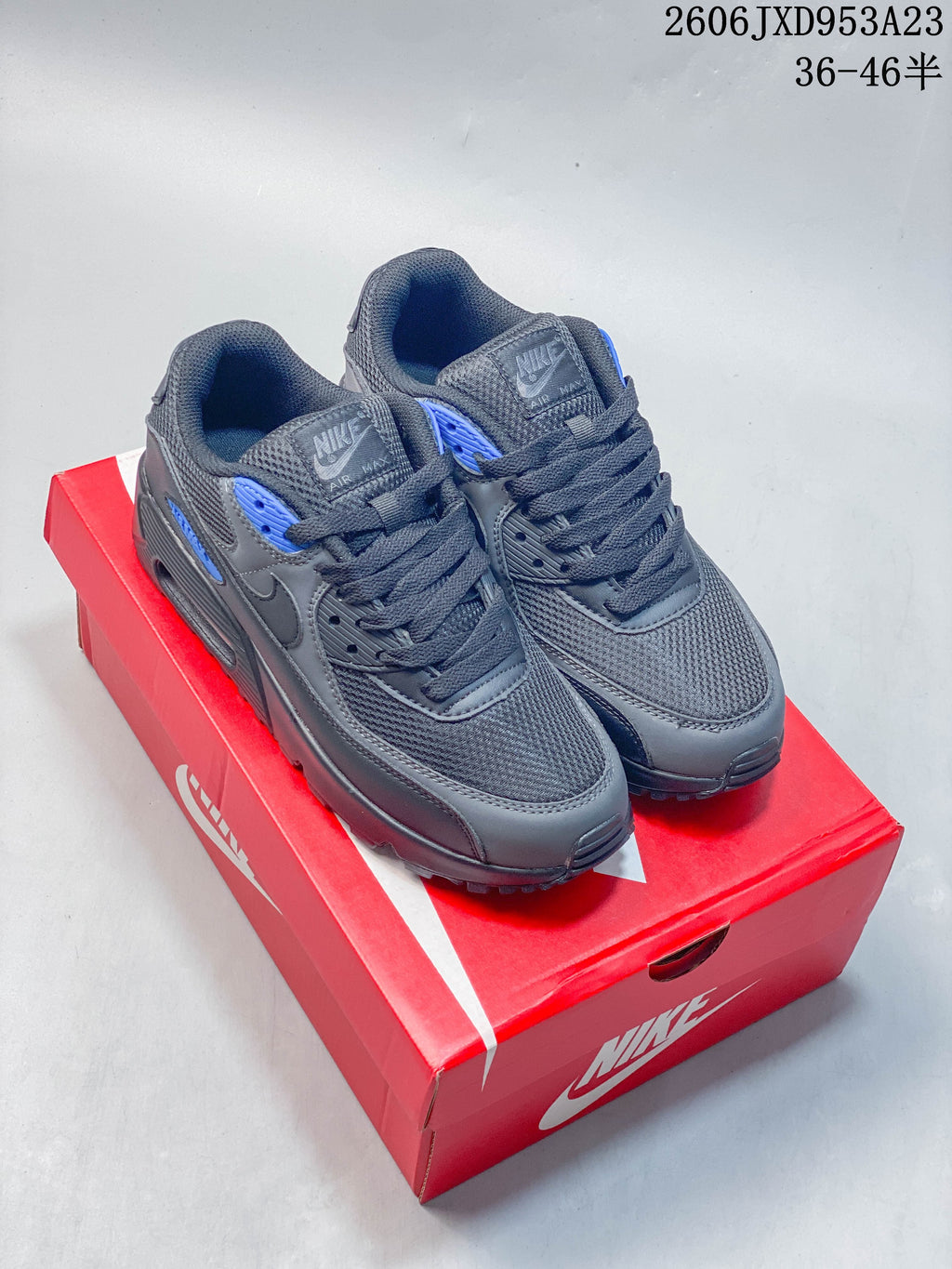 Pair of gray Nike Air Max 90 low-top sneakers with blue accents on a red shoebox