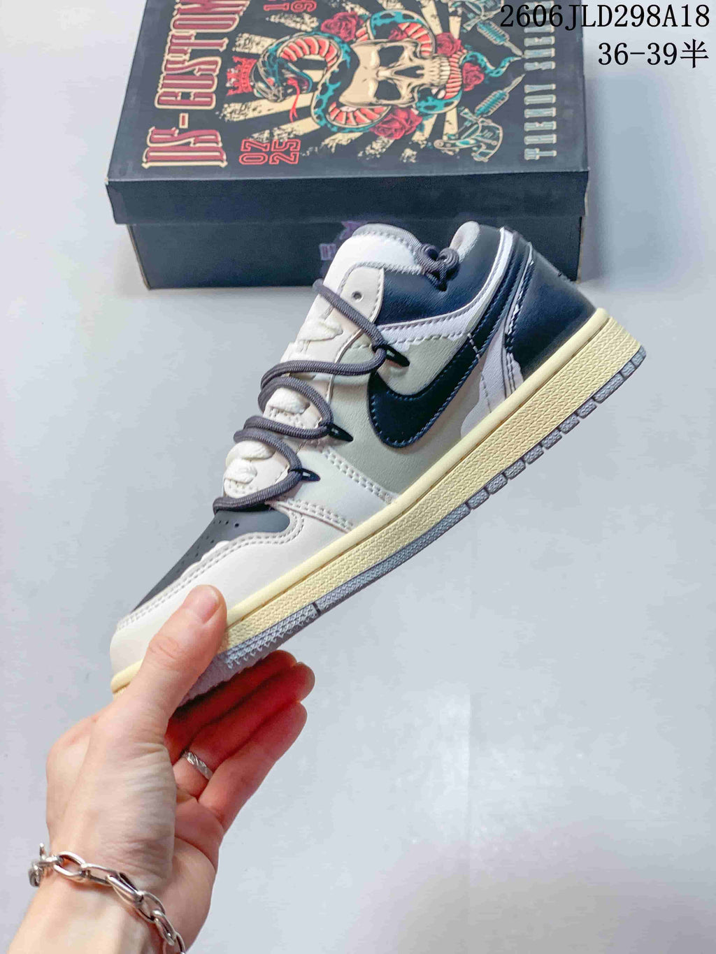 Side profile of a gray and white Air Jordan 1 Low sneaker with a dark Swoosh and layered lacing.