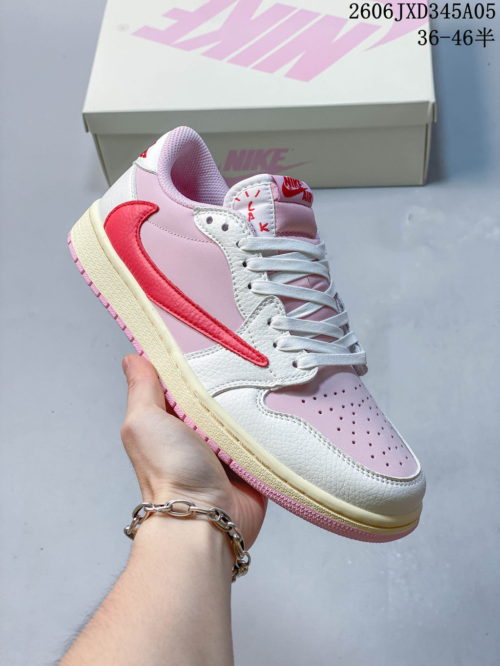 Side view of a white and pale pink low-top sneaker with a bright pink side overlay, held in front of a shoe box.