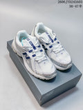 Pair of white and silver New Balance 1906R sneakers with navy accents, shown on a shoebox