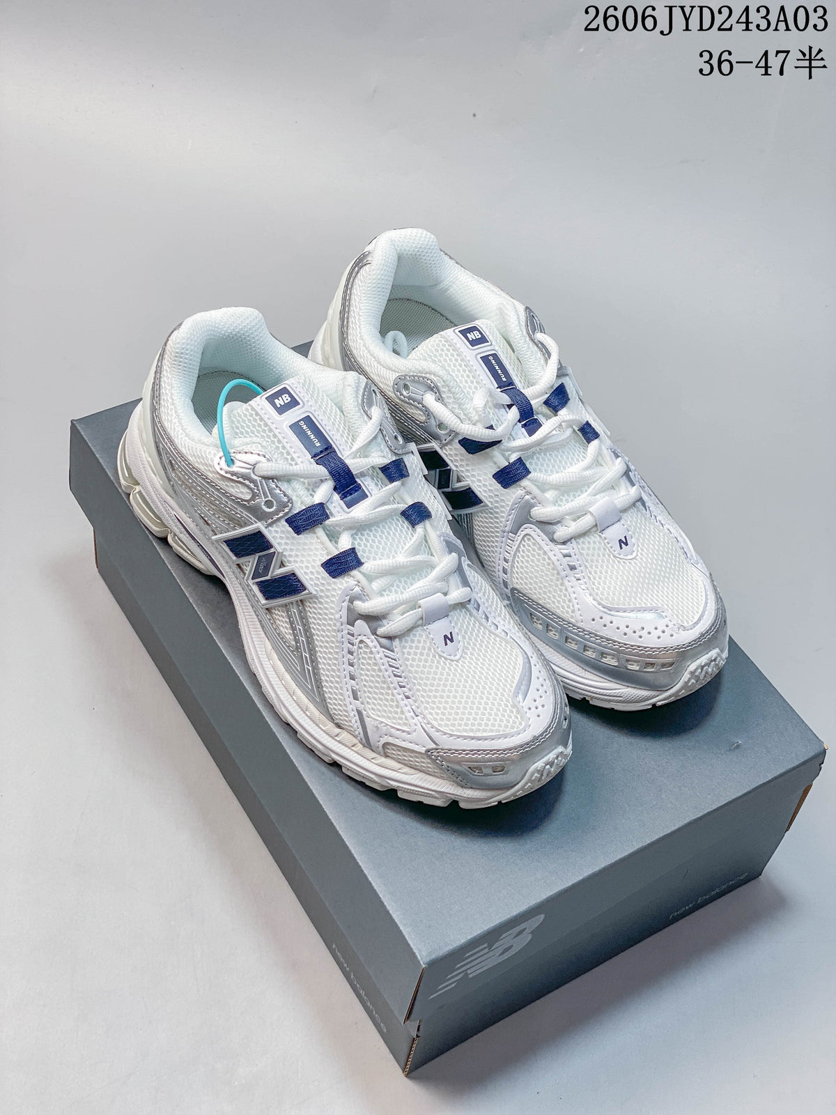 Pair of white and silver New Balance 1906R sneakers with navy accents, shown on a shoebox