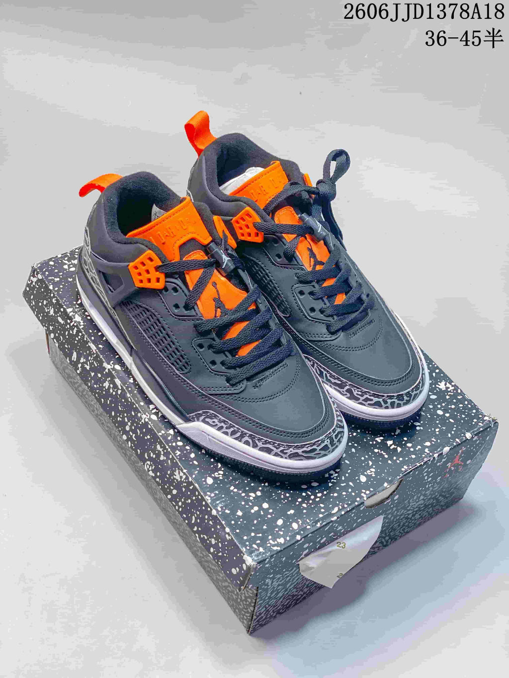 Pair of dark gray Jordan Spizike low-top sneakers with orange accents and elephant-print detailing, shown on a speckled shoebox.