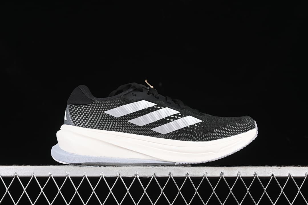 Side profile of a black running shoe with white stripes and a light-colored midsole.