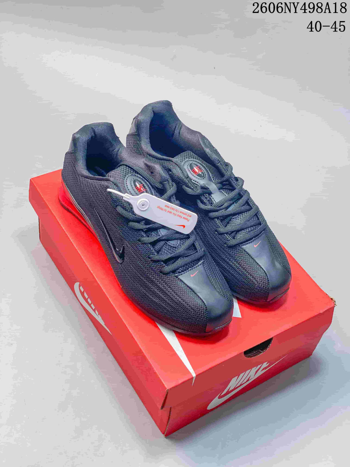 Pair of charcoal Nike Shox TL sneakers with red accents shown on a red shoebox.
