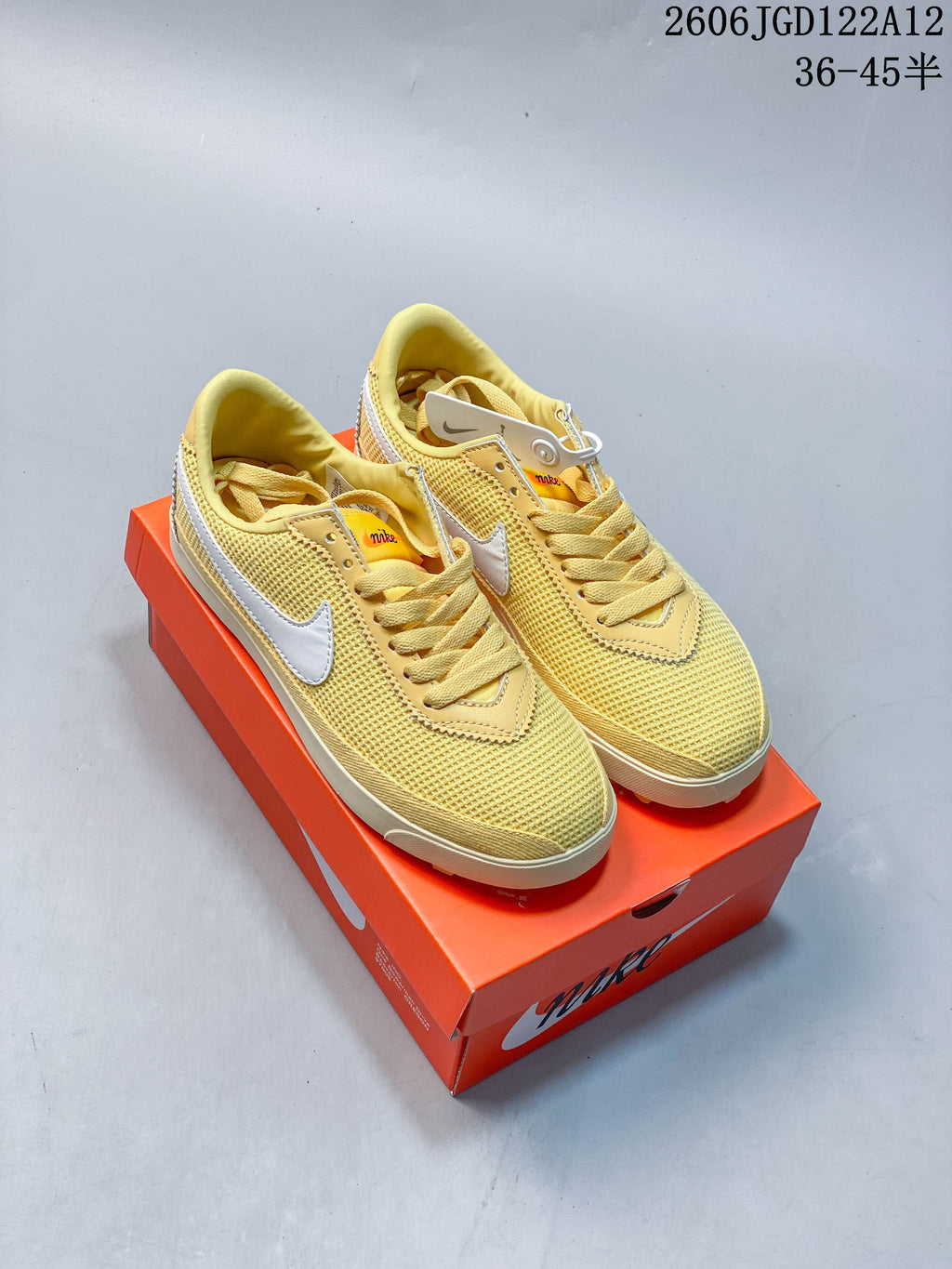 Pair of pale yellow Nike Astro Grabber sneakers with white Swooshes and off-white soles, shown on an orange shoe box.