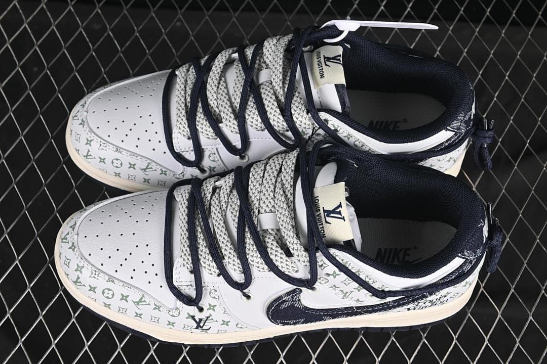 Overhead view of a pair of white Nike SB Dunk sneakers with patterned panels and layered navy and gray laces.