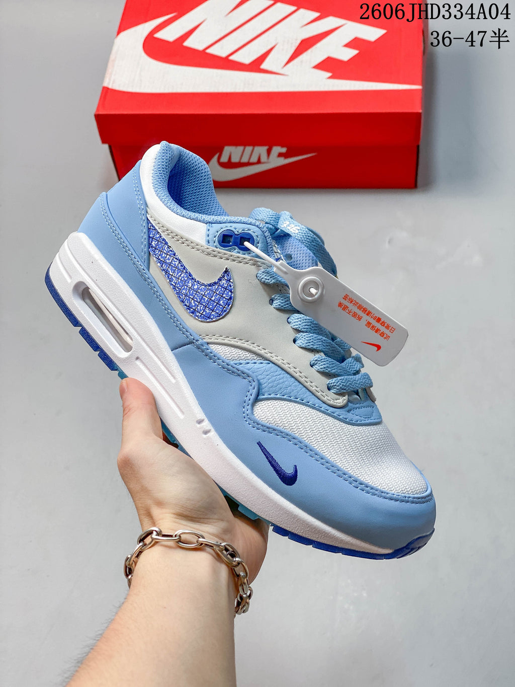 Nike Air Max 1 sneaker in light gray with teal overlays and green Swoosh detailing.