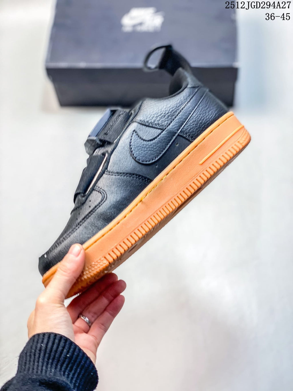 Side view of a black low-top sneaker with strap closure and orange sole
