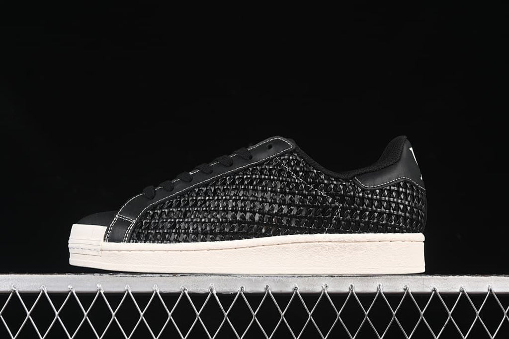 Side view of black adidas Superstar IE8878 sneakers with woven-look panels and an off-white sole