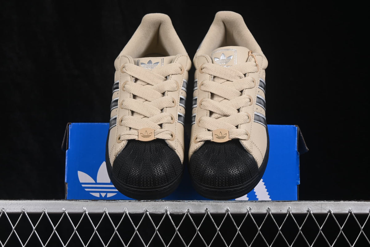 Front view of the pair showing beige laces, black shell toes, silver tongue branding, and three-stripe details.